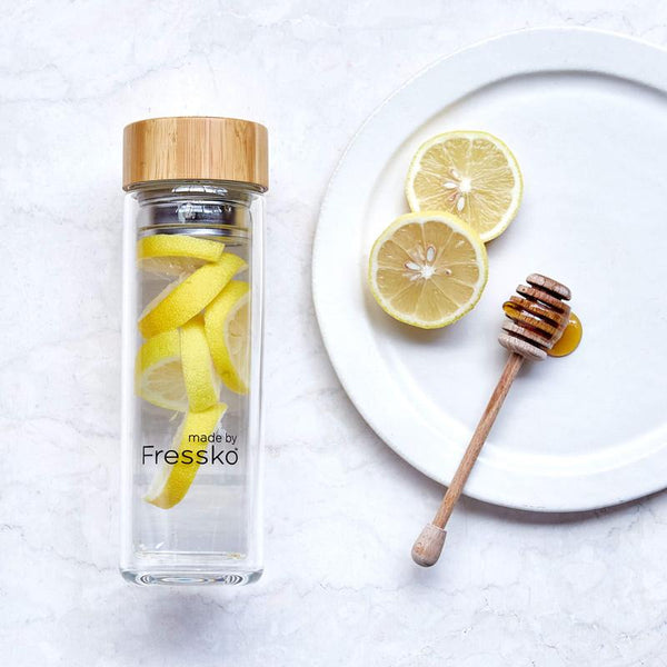 Lemon and honey water in glass fressko flask with plate with lemon and honey next to it