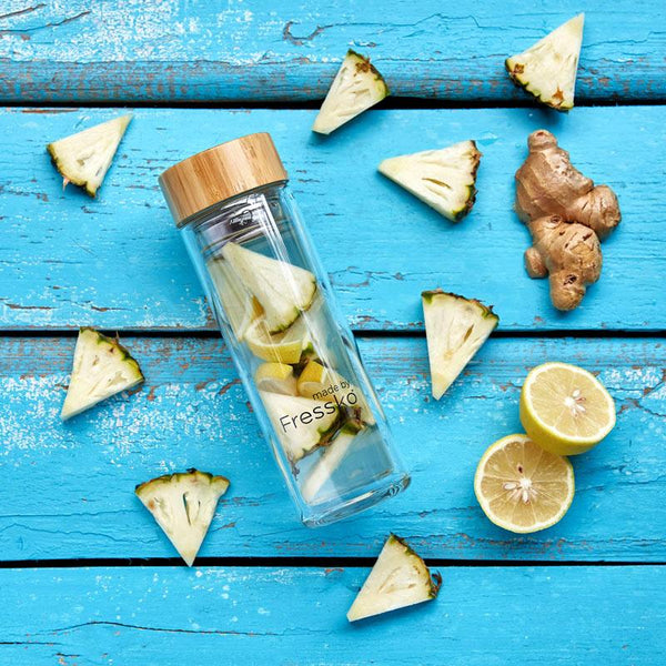 Fruit water in glass fressko flask surrounded by pineapple ginger and lemon